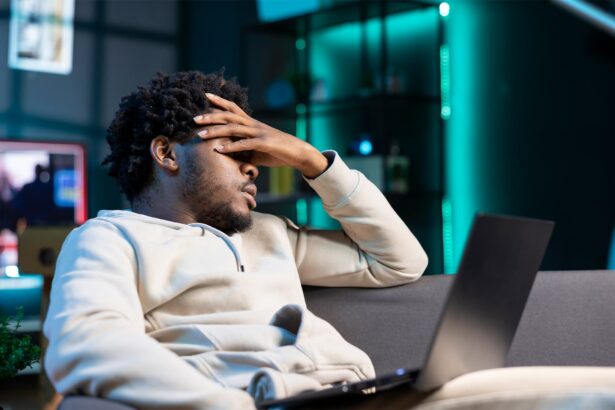 Stellar Photo Recovery Review TrueTech. Man suffering from headache and frustration, sitting on couch at home, after accidentally deleting all his photos from the laptop on his lap.