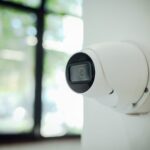 White wall-mounted smart home security camera monitoring a bright window