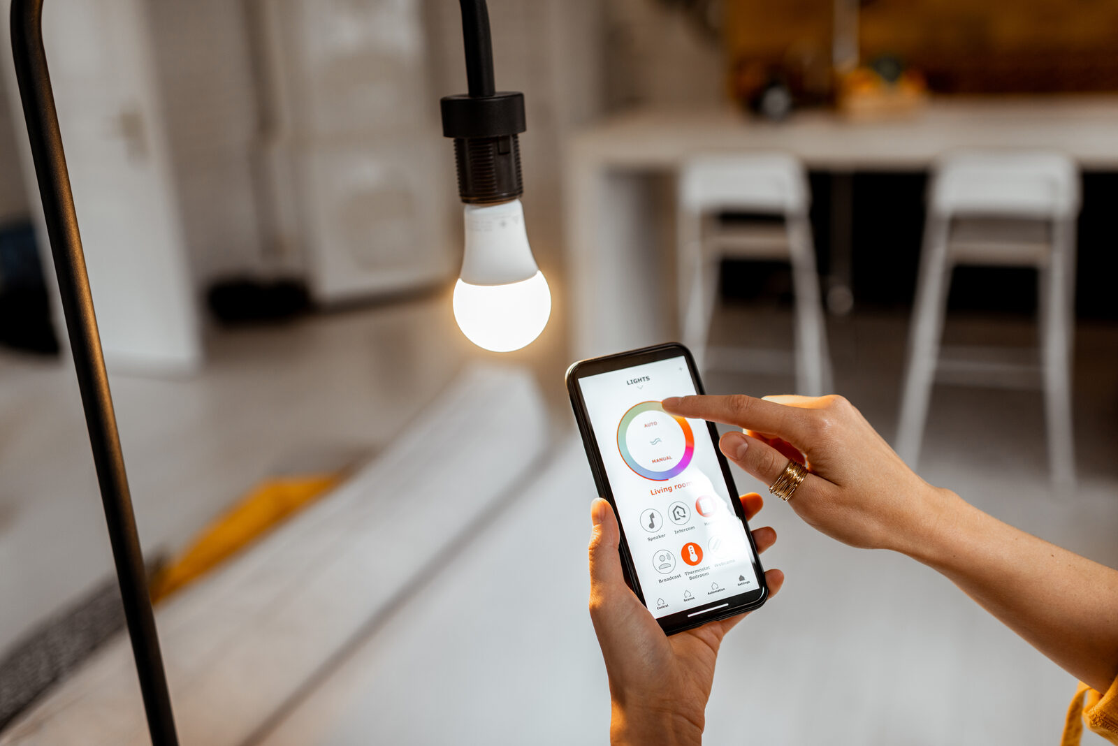 Hand holding a phone running a smart lighting app next to a lit bulb