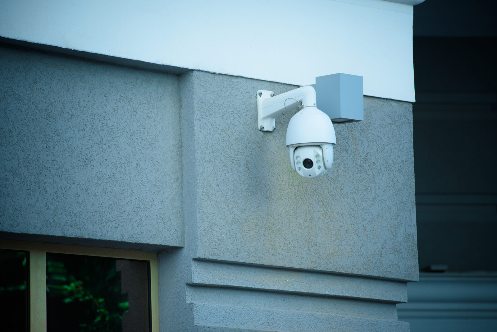 White high-resolution outdoor security camera mounted on a grey building facade