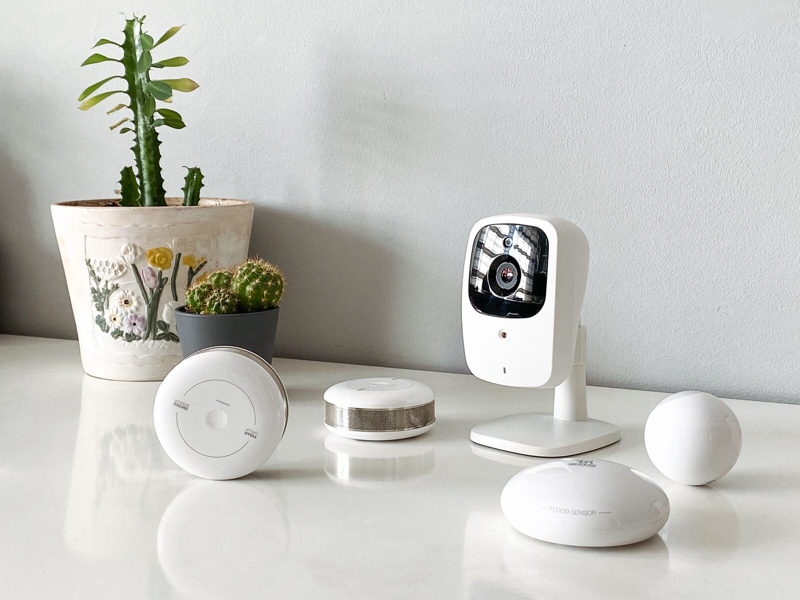 Collection of white smart home devices including a camera, sensors and a hub on a table