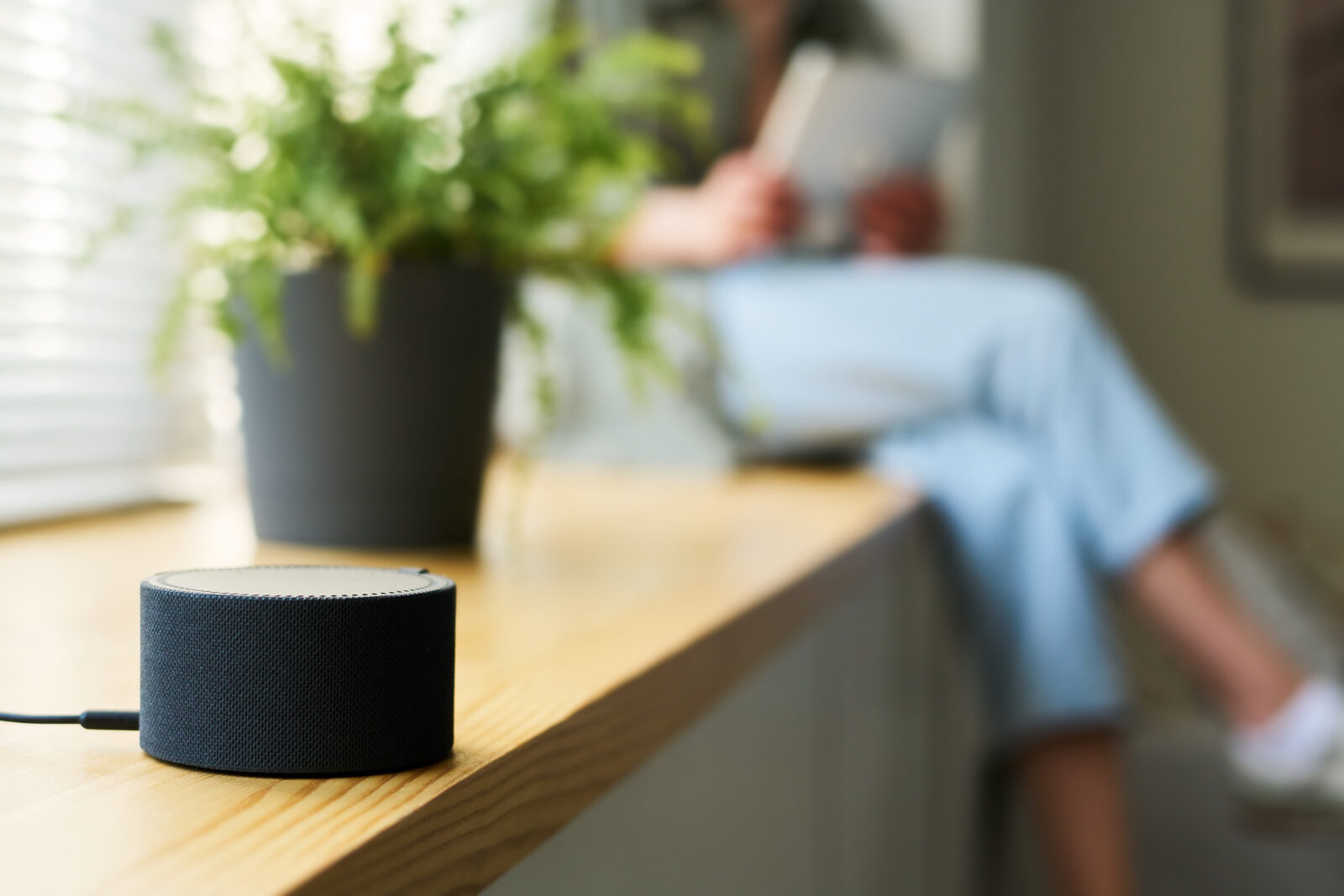 Smart speaker on a wooden ledge with a person using a phone in the background