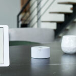 Tablet showing a smart home control panel beside a small white hub on a table