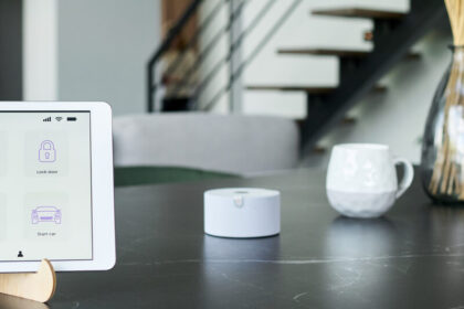Tablet showing a smart home control panel beside a small white hub on a table