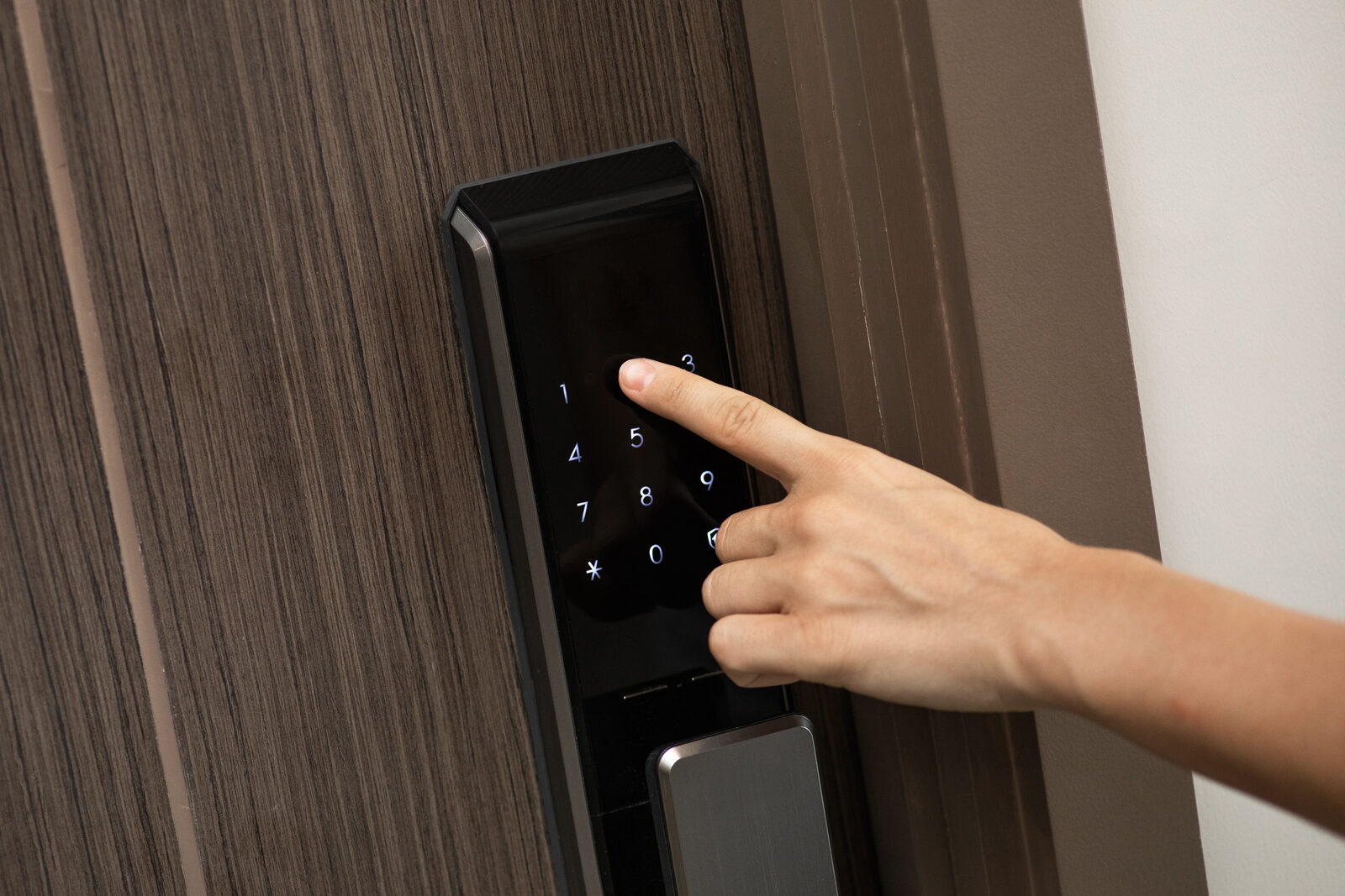 Hand entering a code on a black smart door lock keypad on a modern wooden door
