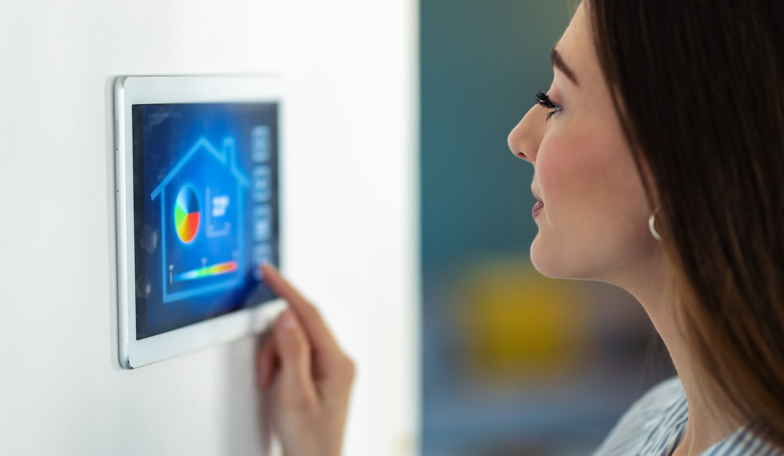 Woman using a wall-mounted smart home automation panel showing a home dashboard