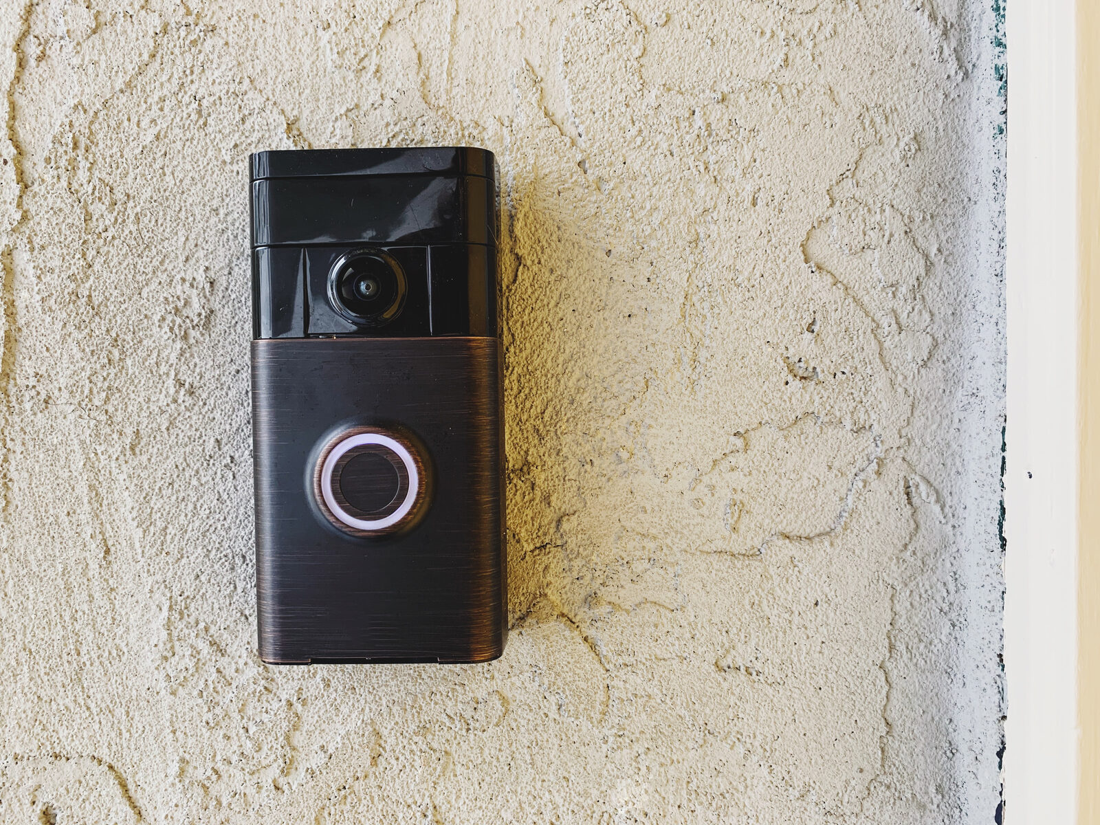 Black smart video doorbell with a camera mounted on a textured exterior wall