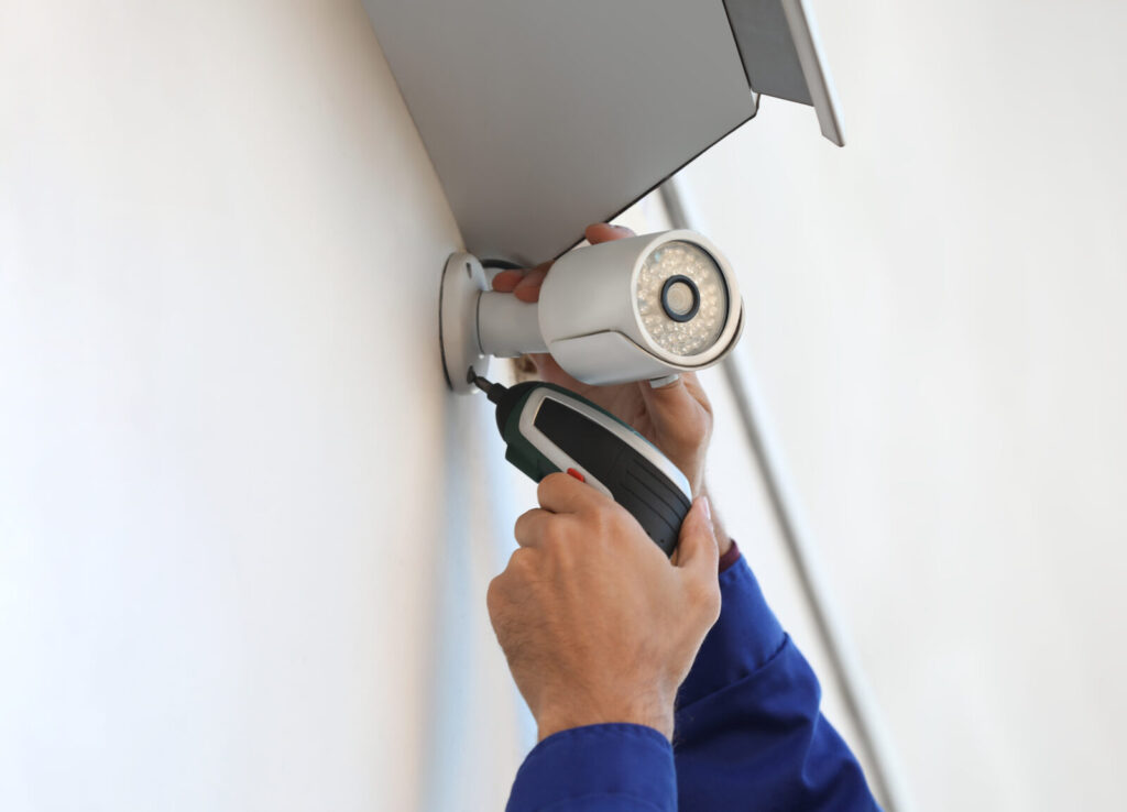 Hands using a cordless drill to mount a wireless security camera on a wall